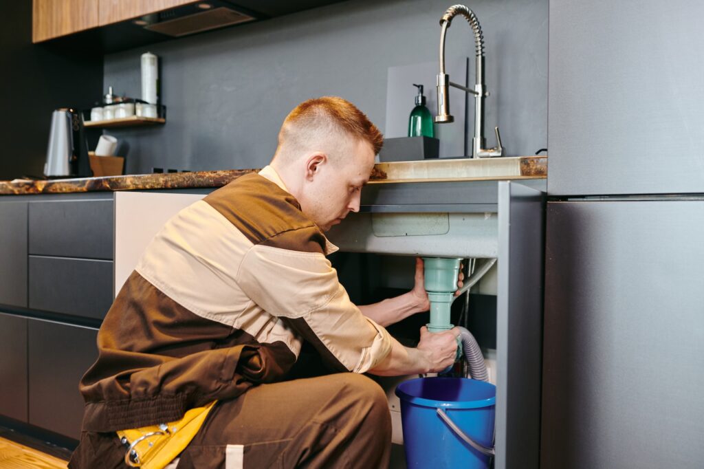 A man in uniform checking plumbing equipment after repairing in the kitchen