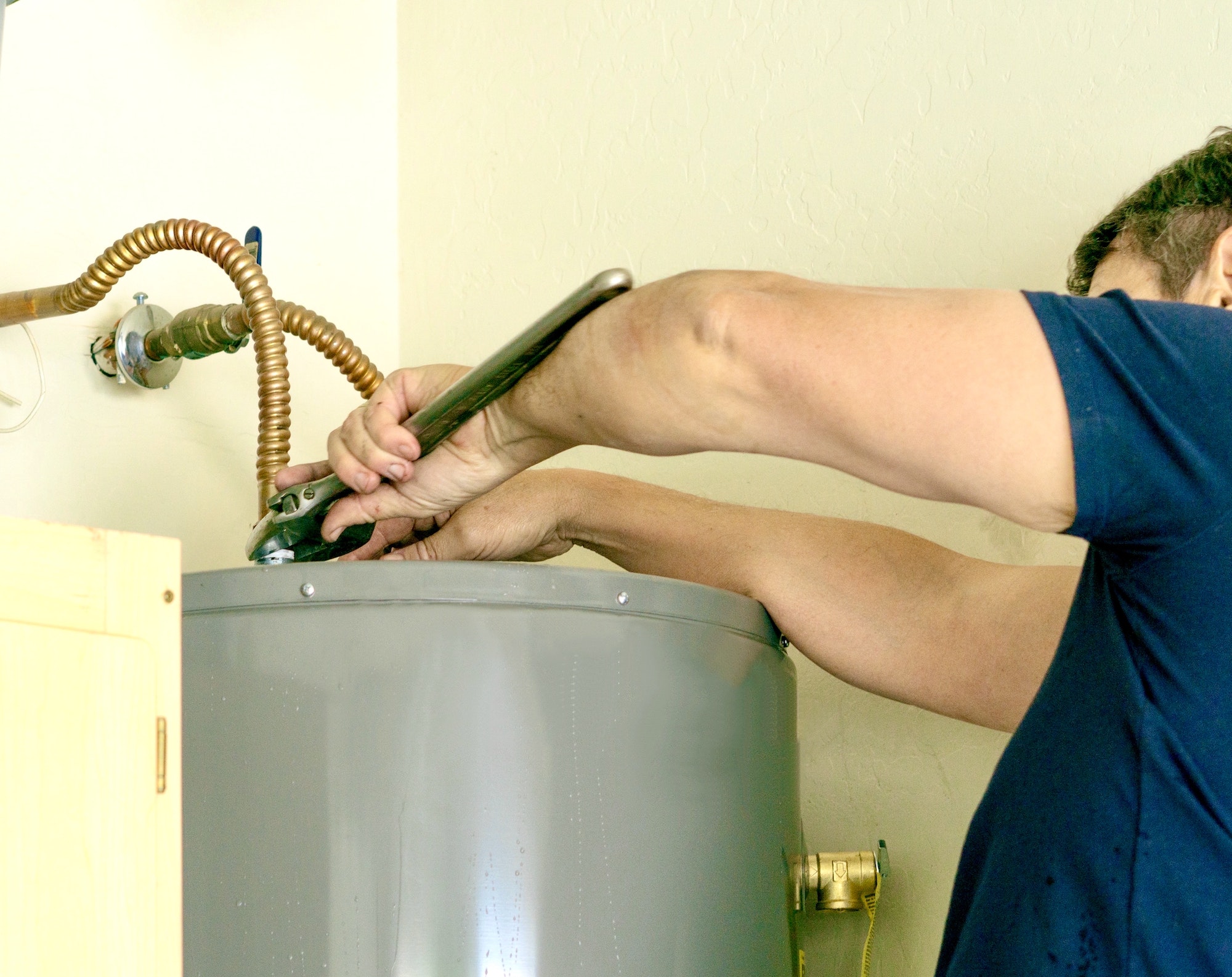 Adult male using a wrench to make adjustments on top of a hot water heater